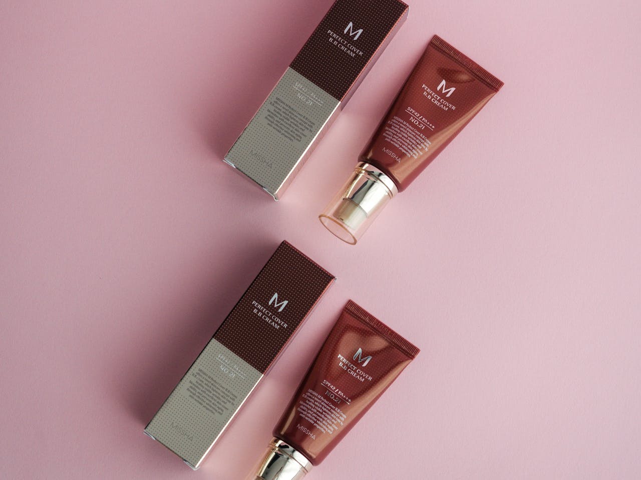 hero-img-01 Flat lay of cosmetic products on a pink surface featuring foundation creams.