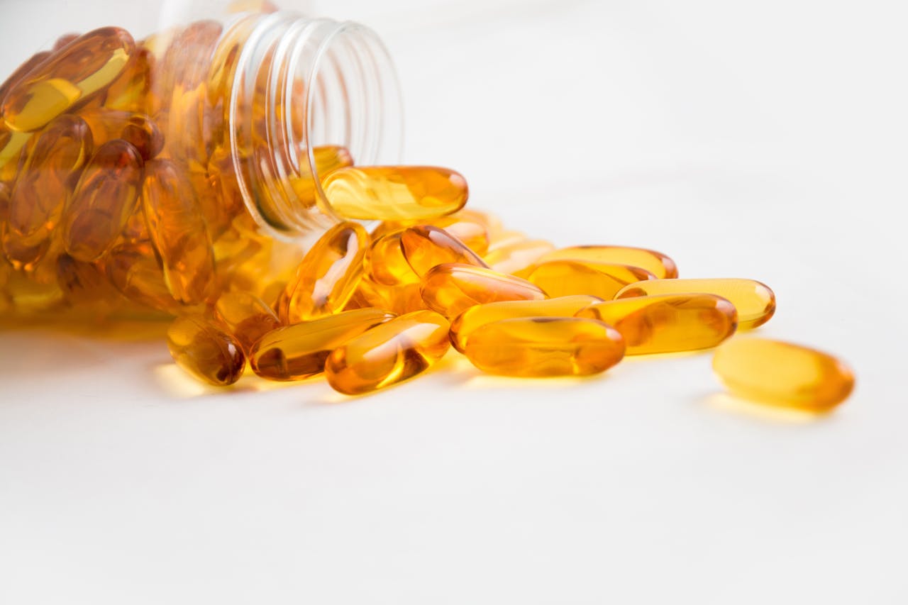 services-01 Close-up of fish oil capsules spilling from a bottle on white background.