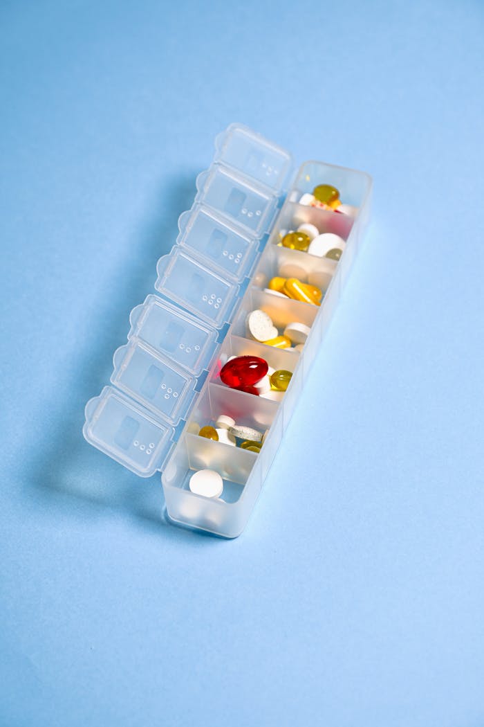 services-img Colorful pills and capsules organized in a weekly pill container against a blue background.