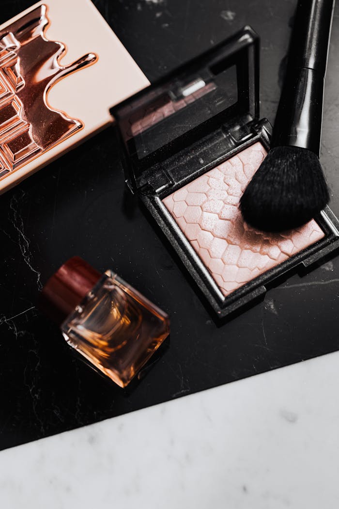 gallery-3 Stylish flat lay of makeup products including highlighter, brush, and perfume bottle on marble surface.